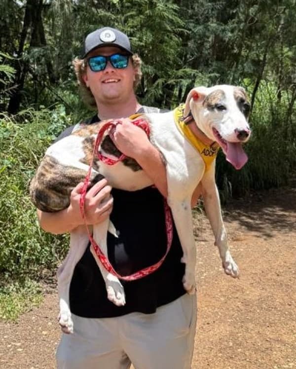 Kruz Merrill on a trail, carrying a rescue dog wearing an ADOPT bandana